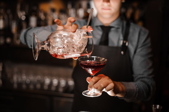 Bartender pouring a red alcoholic cocktail into the glass