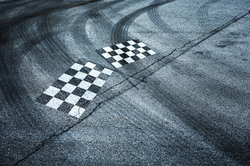 Checkered flags painted on race asphalt road with crossing of tires tracks.