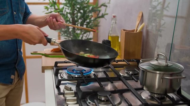 Nice man cooking different healthy vegetables in wok. He is turning wok with special movements so vegetables flip.