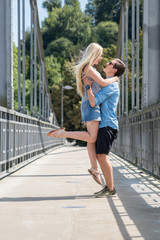 Junger Mann hebt seine Freundin auf einer Brücke hoch
