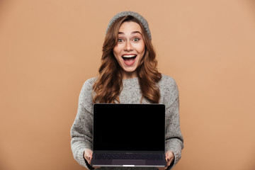 Portrait of happy exited brunette woman holding and showing blank laptop screen