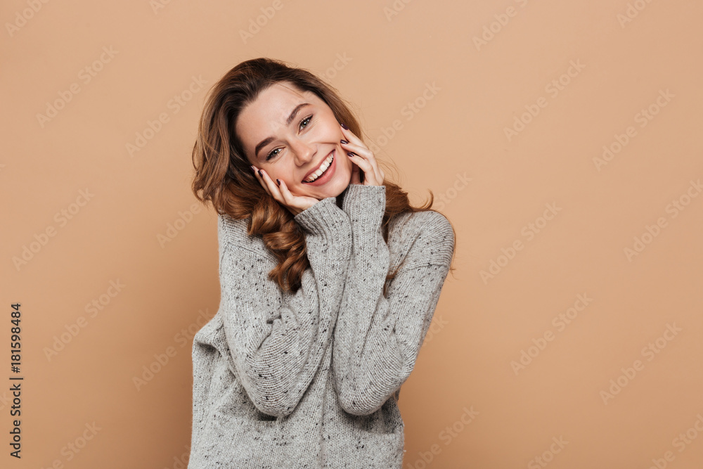 Sticker Portrait of cute smiling brunette girl in soft sweater touching her face while looking at camera