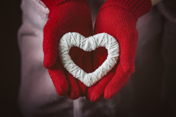 A girl in red gloves holds a heart. Flat lay