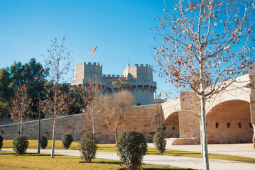 A view from Turia park gardens to  Serranos Gate with a flag, famous Valencian Towers, part of the ancient city wall, and a roman bridge at the foreground on autumn winter sunny day.