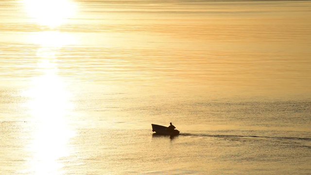 pescatore passacon la sua barca alle prime luci dell'alba con il mare color oro