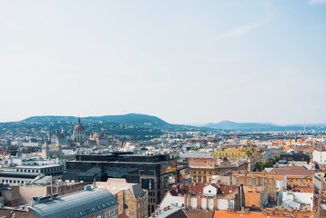 Beautiful panoramic aerial view over the roofs of Budapest, old orange tile roofs and Parliament building with blue hills and forest at the background on sunny summer day, Hungary. Copy space.