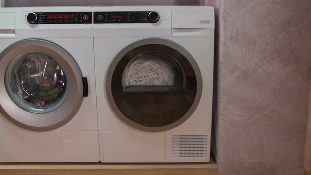 Advanced machines working in nice and tidy utility room. Dryer is working at full speed, washing machine is washing laundry.
