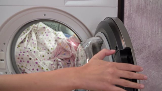 Woman gently opening dryer and taking dry clothes out. These light coloured clothes belong to all family members.