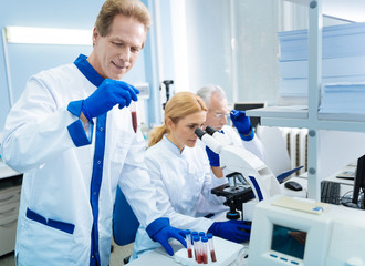Analysis going well. Happy smiling researcher holding a test tube and looking at it while a blond...