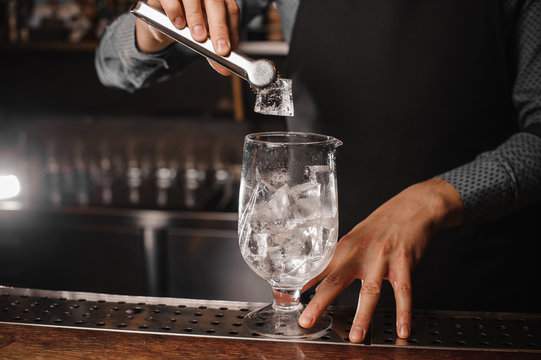 Barman putting ice cubes into the cocktail glass