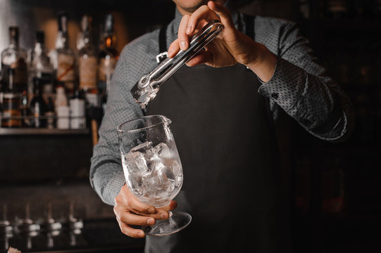 Barman adding ice cubes into the cocktail glass