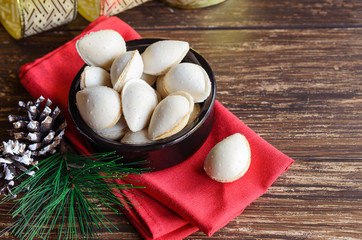 Spanish dessert, almendras rellenas, almond crisps filled with turron cream in the ceramic bowl with christmas decoration on wooden table. Traditional Christmas sweets in Spain.