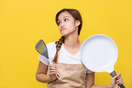 Young woman holding a frying pan and a spatula.