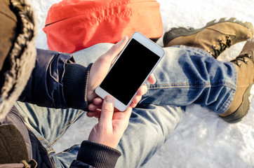 Hipster business man sitting in snow using white mobile smart phone, oled display, on wild nature,...