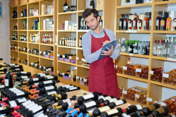 joyful male seller in uniform holding clipboard in wine shop