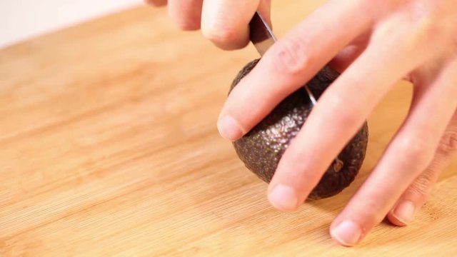 Hands cutting an avocado.