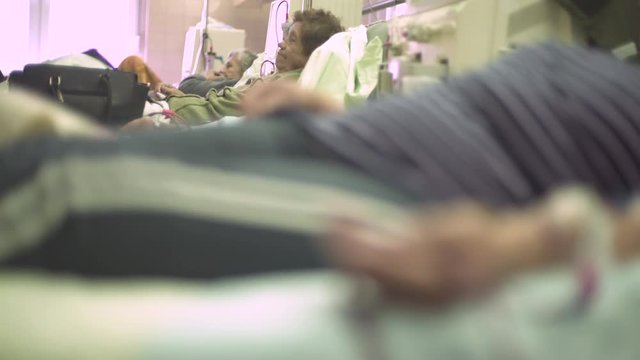 Mature female patients lying in the beds during hemodialysis treatment, focus change from portrait of elderly woman to hand during blood flows through the tube injected in vein, macro shot, real scene