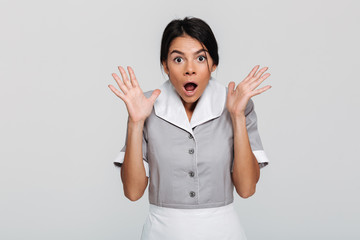 Close-up photo of amazed brunette maid in uniform standing with opened palms and looking at camera