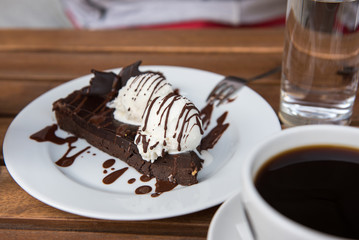 Brownie cake with vanilla ice cream served with coffee on white plate 
