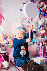 Fototapeta na wymiar Little boy plays with toys before a white Chritmas tree with pink and blue toys