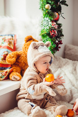 Little boy in bear suit holds an orange sitting on the floor