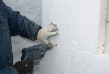 Builder drilling wall for installing anchors to hold rigid insulation foam board. How to attach rigid foam insulation to a concrete wall - obrazy, fototapety, plakaty