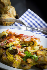 Gröstl von Semmelknödeln mit Pilzen und Speck mit karierter Serviette und Besteck im Hintergrund