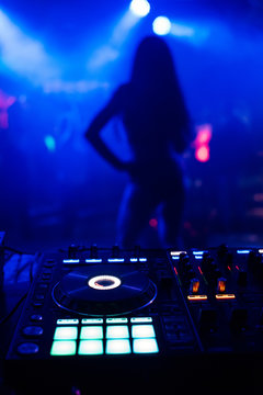 silhouette of young slim dancers on stage out of focus through the DJ booth and a mixer