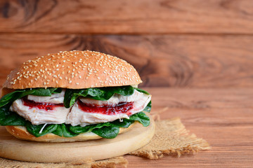 Homemade chicken breast burger. Tasty chicken burger with fresh spinach and berry jam on a wooden board. Wooden background with copy space