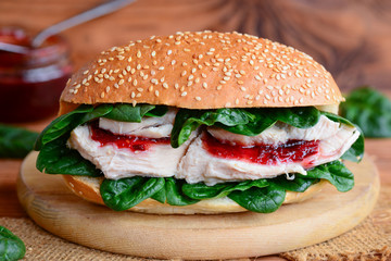 Crispy chicken fillet burger recipe. Simple chicken burger with fresh spinach and berry jam on a wooden board. Closeup
