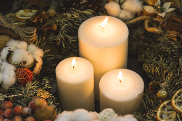 Big white christmas candles in a pine wreath decorated with berries and pinecones
