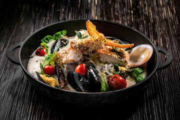 Bowl of delicious seafood meal with rice noodles. Meal made of sea bass fish, mussels, crab meat and other seafood with vegetables on a table.