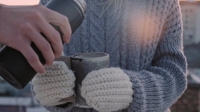 Slow motion shot of cute girl in grey knitted wool sweater and white mittens, hold artisan big mug or cup while someone pours hot tea or coffee to warm her up on cold winter day