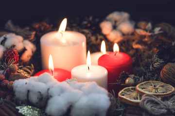 Big red and white burning wax candles in a pine christmas wreath