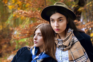 Fashion portrait of two beautiful women in autumn landscape. Trendy woolen coat and scarf. Fashion autumn concept.Closeup.Brunette and blonde