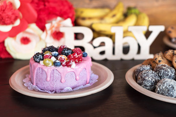 Birthday cake and muffins with wooden greeting sign on dark background. Wooden sing with letters Baby and holiday sweets.