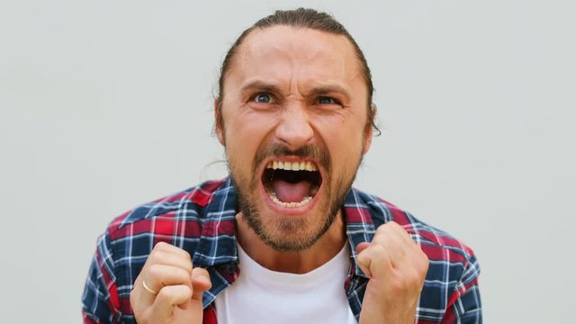 Close up shot of angry emotional young man in the denim shirt screaming and waving with his hands on the white background.