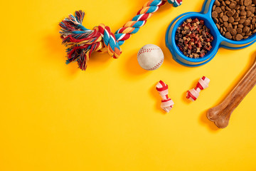 Toys -multi coloured rope, ball and dry food. Accessories for play on yellow background top view