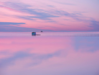 A small wooden house on the water's edge with the reflection of the sky in the water. Calm calm relaxing look on the evening sunset of the water surface and a lonely structure on the water.
