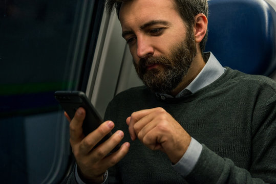 Youn adul man commuter businessman seated on train look at smartphone during travel in the evening.