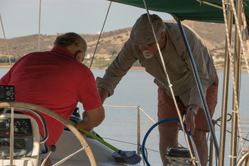 Two old friends are sailing & cleaning deck of a yacht together.  Concept: active elderly people. 