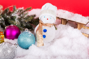 snowman on white snow with cyan and silver baubles, green christmas tree and sleigh. red background