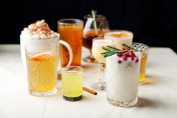 Set of various winter cocktails: mulled wine, eggnog, limoncello, old-fashioned, coconut margarita. Black background, white linen tablecloth.