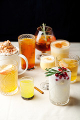 Set of various winter cocktails: mulled wine, eggnog, limoncello, old-fashioned, coconut margarita. Black background, white linen tablecloth. Vertical composition. Copy space.