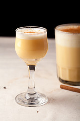 Two glasses with christmas eggnog drink decorated with cinnamon on dark background. Vertical composition.