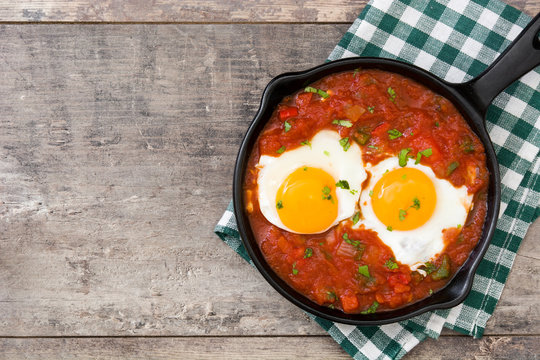 Mexican breakfast: Huevos rancheros in iron frying pan on wooden table top view copyspace