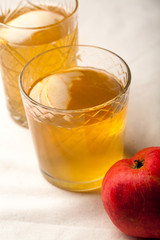 Two vintage glasses with apple cider on black background. Christmas beverages concept. Two red apples and rosemary sprig aside.  Warm backlight. Vertical composition.
