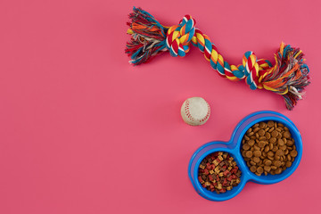 Toys -multi coloured rope, ball and dry food. Accessories for play on pink background top view