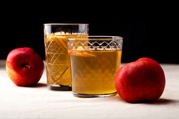 Two vintage glasses with apple cider on black background. Christmas beverages concept. Two red apples and rosemary sprig aside.  Warm backlight. Horizontal composition. Side view.