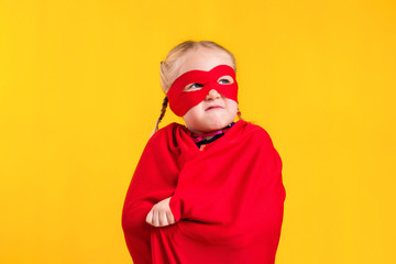 Fototapeta na wymiar Funny little power superhero child girl in a red raincoat and a mask. Superhero concept.